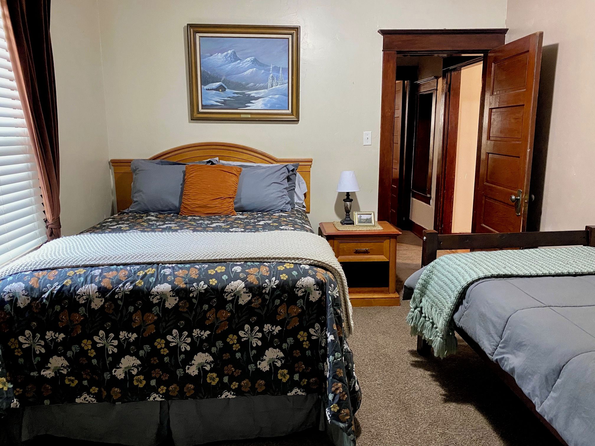 A bedroom with a bed, bedside table, lamp, and a painting on the wall.