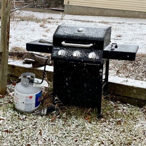 Un barbecue portatif avec une bouteille de propane, installé sur une pelouse où la neige recouvre le sol.