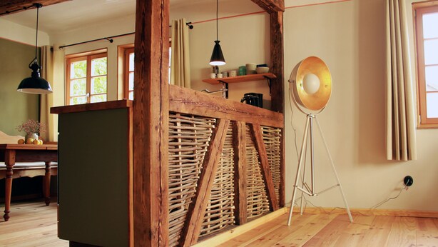 A room with a wooden ceiling, a green cabinet, a tripod lamp, and a window with curtains.