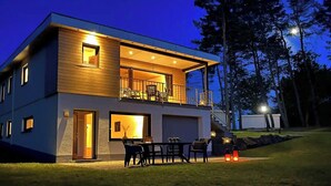 Una casa moderna de dos pisos con un balcón, un comedor con mobiliario exterior y un garaje.
