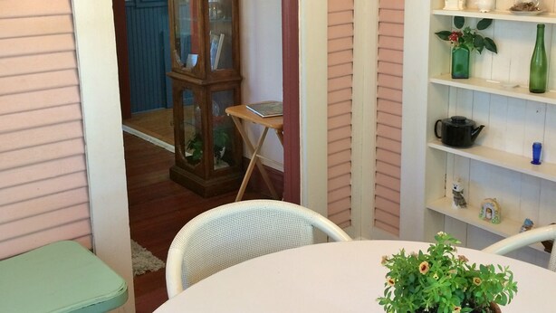 Ett rum med ett runt bord, en krukväxt, ett träskåp och en hylla med gröna flaskor.