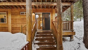 A wooden staircase leading to a cabin entrance with snow on the steps.