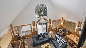 A cozy loft-style living area with a large arched window, wooden walls, and a mix of seating options including a sofa and a couch.