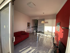 En moderne stue med en rød sofa, et glasbord og et køkken i baggrunden.