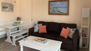 Un salon chaleureux avec un canapé marron, une table basse blanche et un tableau représentant une scène de plage.