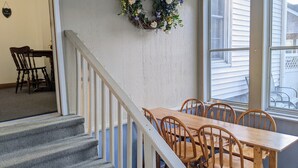 Un comedor con una mesa y sillas de madera, una escalera con barandilla blanca y un arreglo floral en la pared.