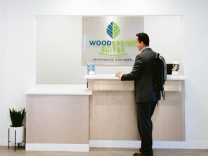 Un hombre en la recepción de un hotel, con un cartel que dice "WOODSPRING SUITES AN EXTENDED STAY HOTEL".