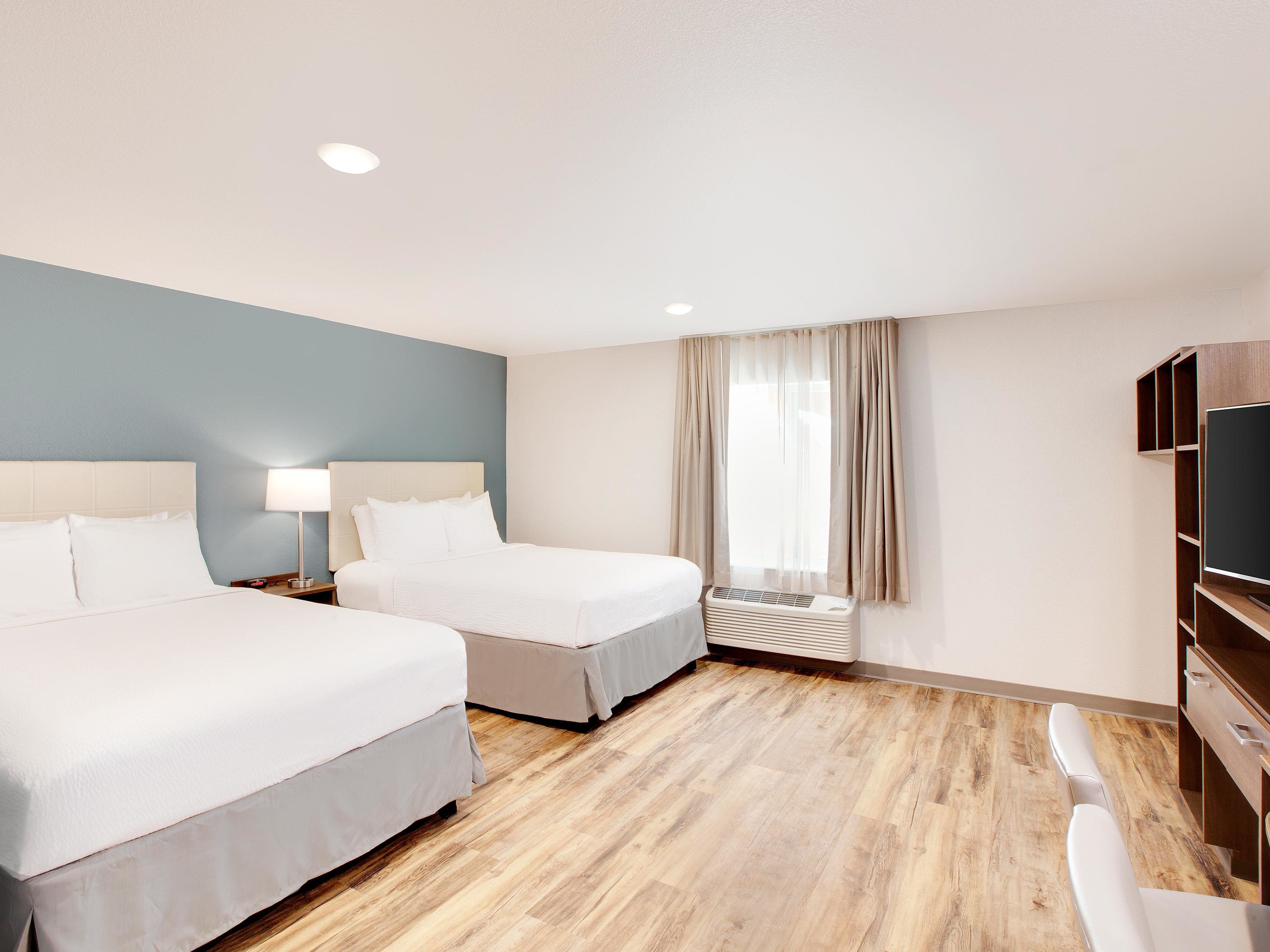 A hotel room with two beds, a TV, a desk, and a window with curtains.