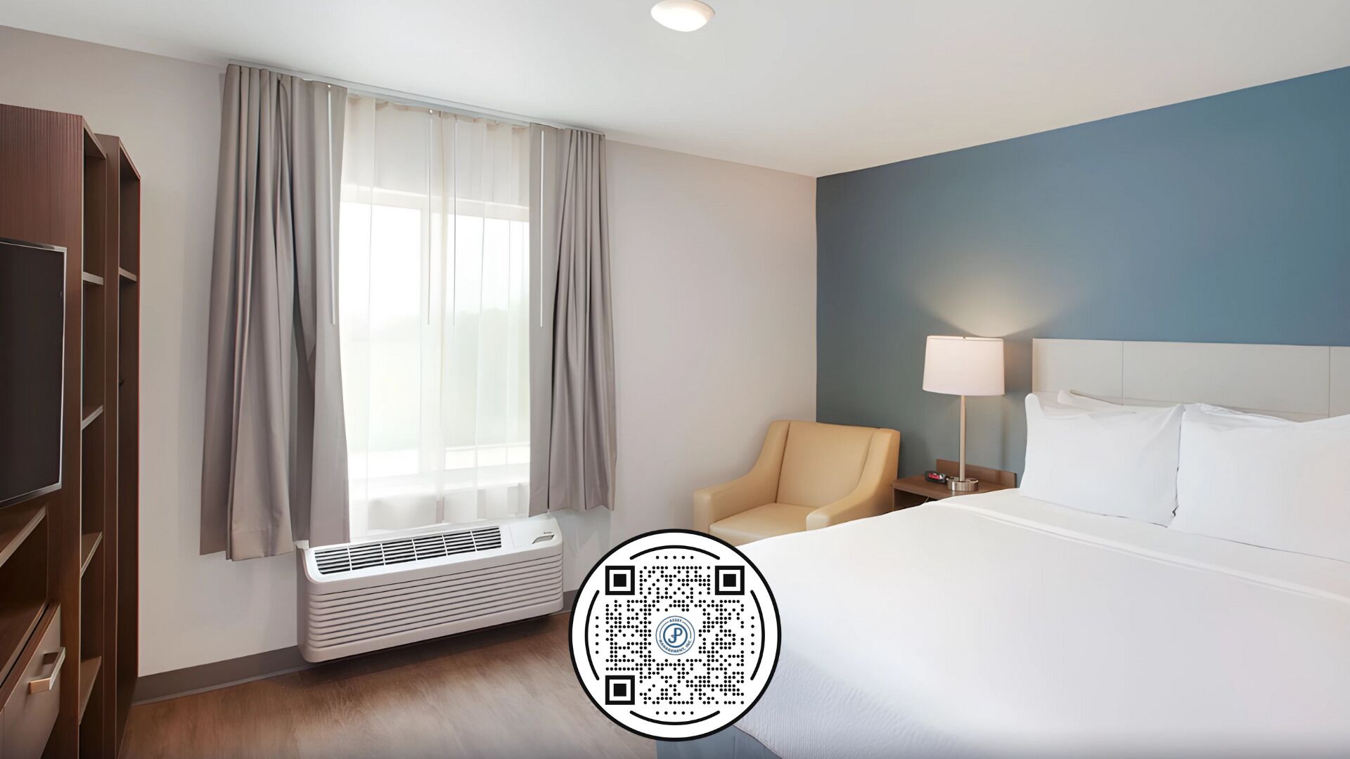 Una camera d'albergo con un letto, una sedia, una scrivania con una lampada, una televisione e una finestra con tende.