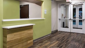 Zona de recepción con pared verde, mostrador de madera y puerta de cristal.