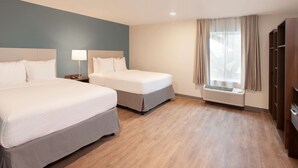 Habitación de hotel con dos camas, una mesita de noche con lámpara, ventana con cortinas y aire acondicionado instalado.