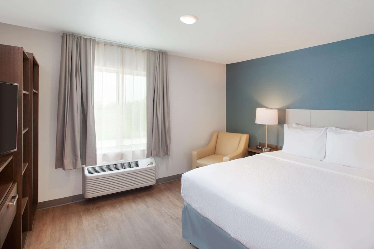 Ein Hotelzimmer mit Bett, Sessel, Schreibtisch, Lampe und Fernseher.