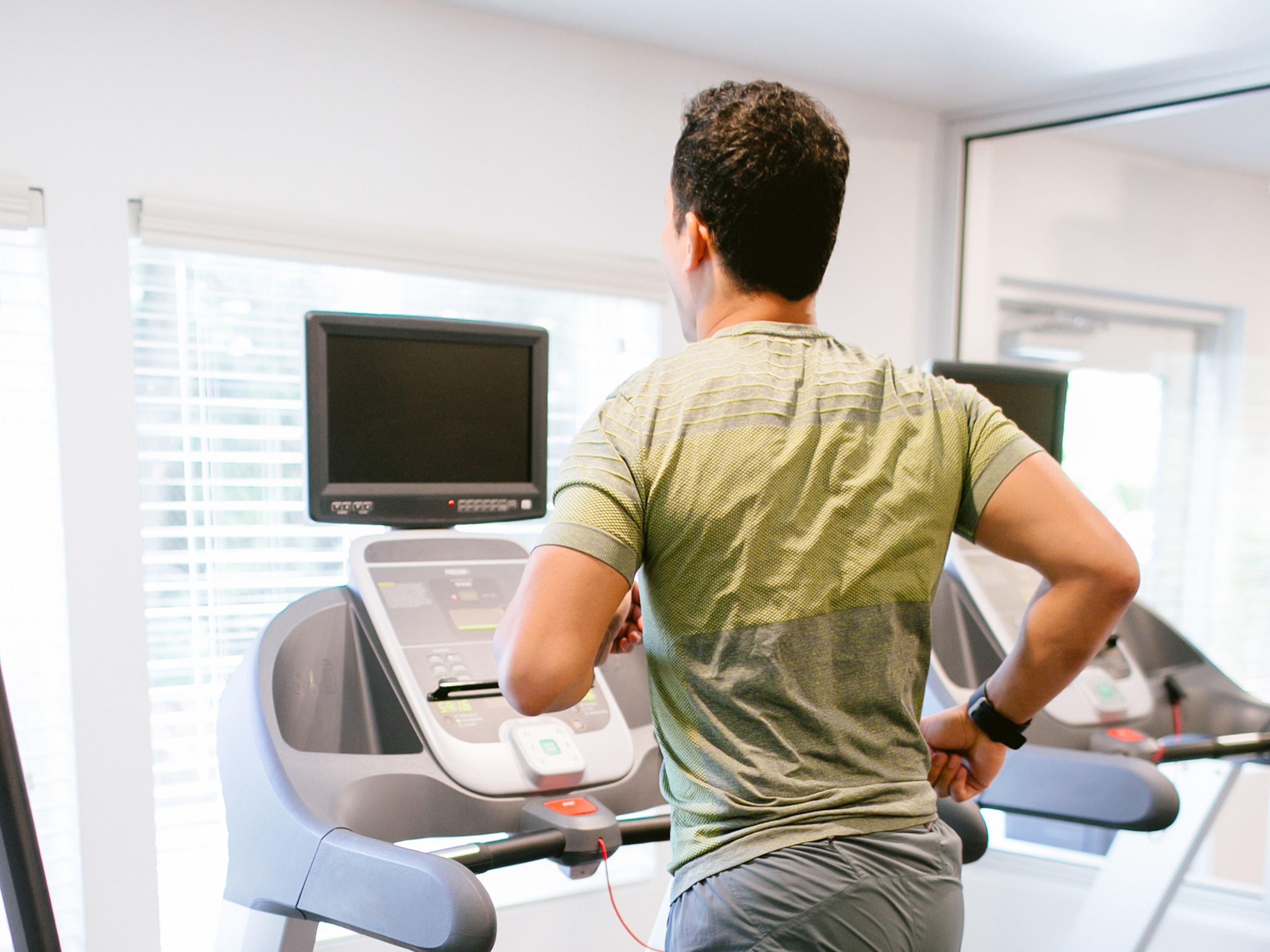 Une personne utilise un tapis de course dans une salle de sport, qui est équipé d’un écran numérique et de fenêtres.