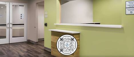 A reception area with a green wall, a white reception desk, and a QR code on the wall.