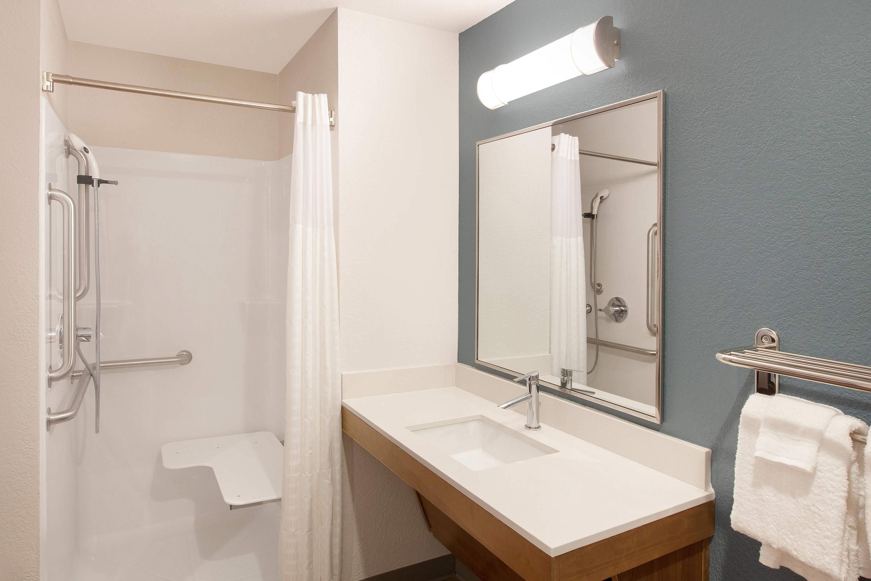Un baño con ducha, lavabo, espejo y toallero.