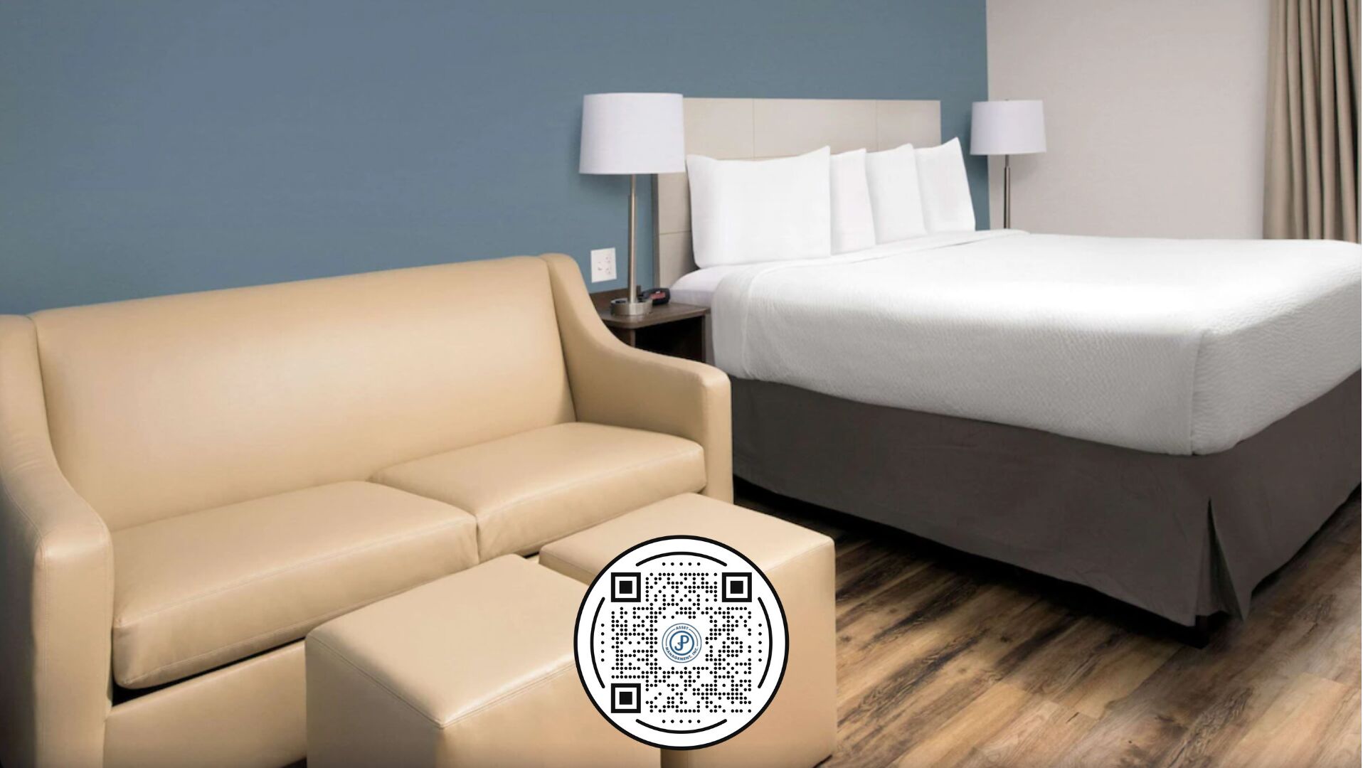 Et hotelværelse med en beige sofa, en seng med hvide sengetæger og trægulv.