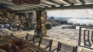 Un patio al aire libre con paredes de piedra, muebles de mimbre y vista al mar.