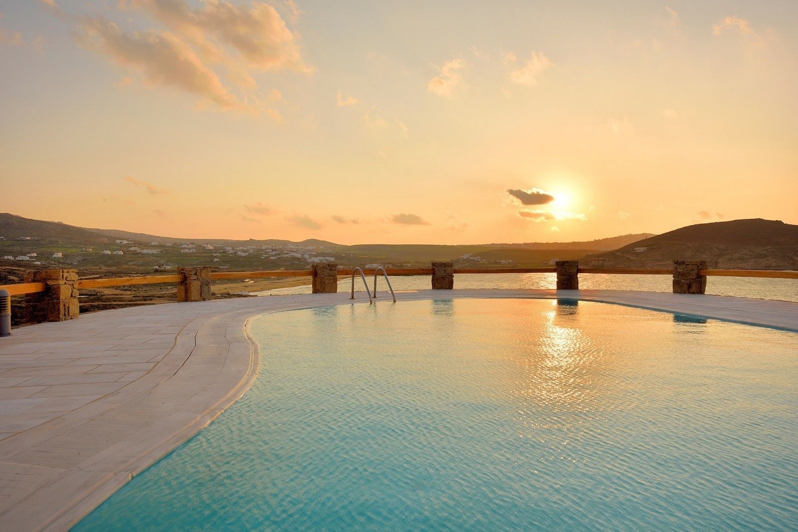 A swimming pool with stone pillars, a stone deck, and a sunset view.