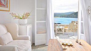 A room with a white sofa, a wooden table with glasses, and a view of the sea. - Villa Juliet (Mykonos)