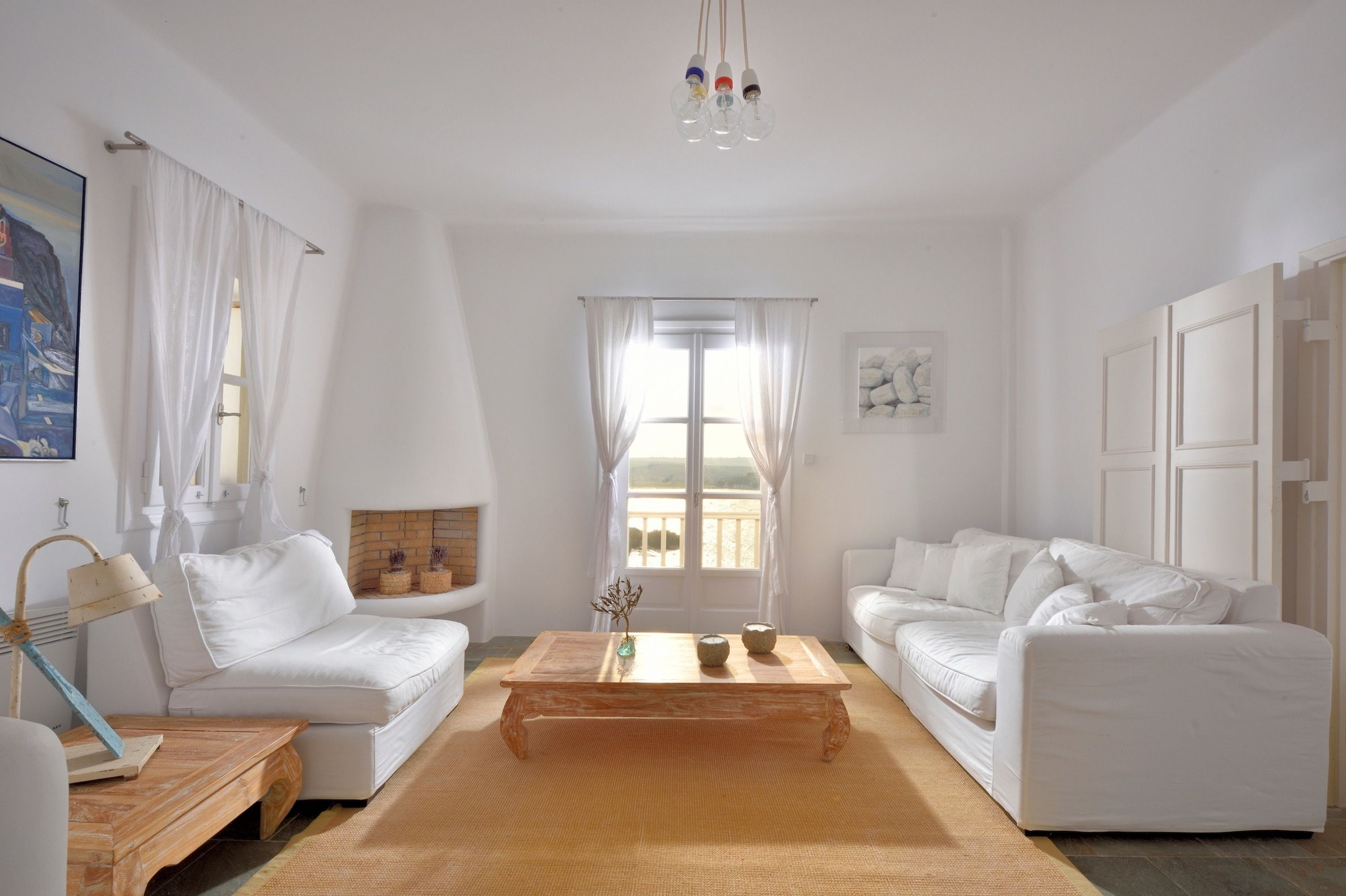 Ein hell eingerichtetes Wohnzimmer mit zwei weißen Sofas, einem Holztisch und einem großen Fenster mit Vorhängen.