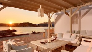 A covered outdoor seating area with white furniture, a table, and a hanging light fixture. - Villa Juliet (Mykonos)