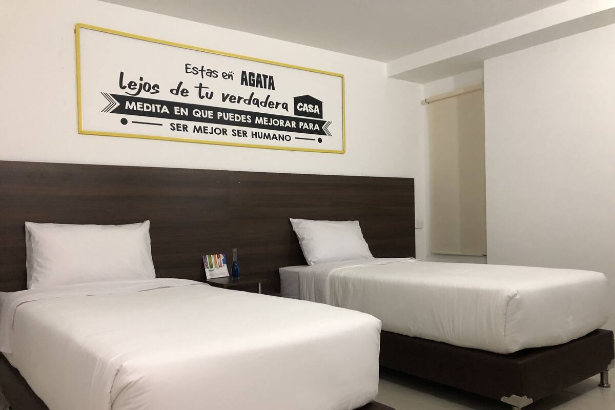 A hotel room with two beds, a dark wooden headboard, and a motivational quote on the wall.
