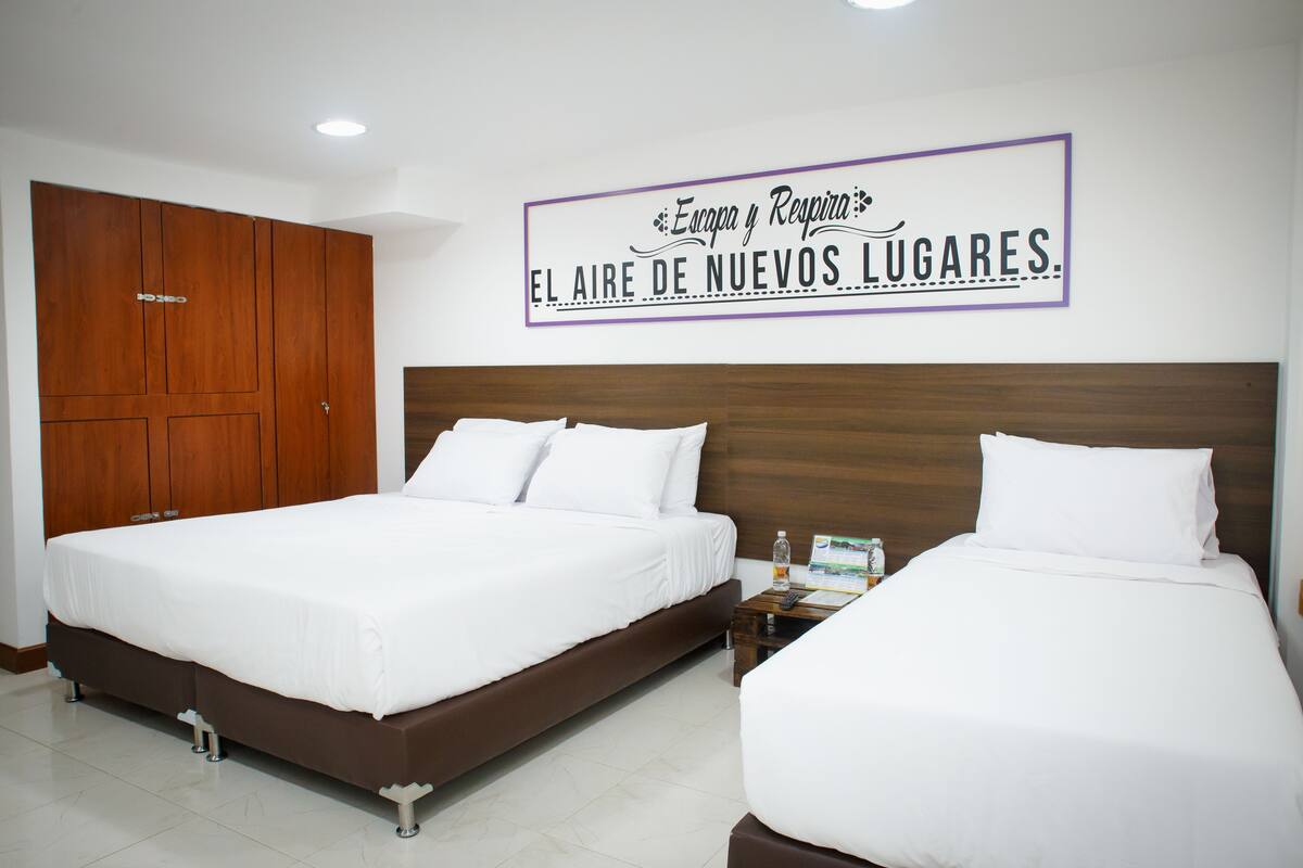 A hotel room with two beds, wooden wardrobe, and a sign on the wall.