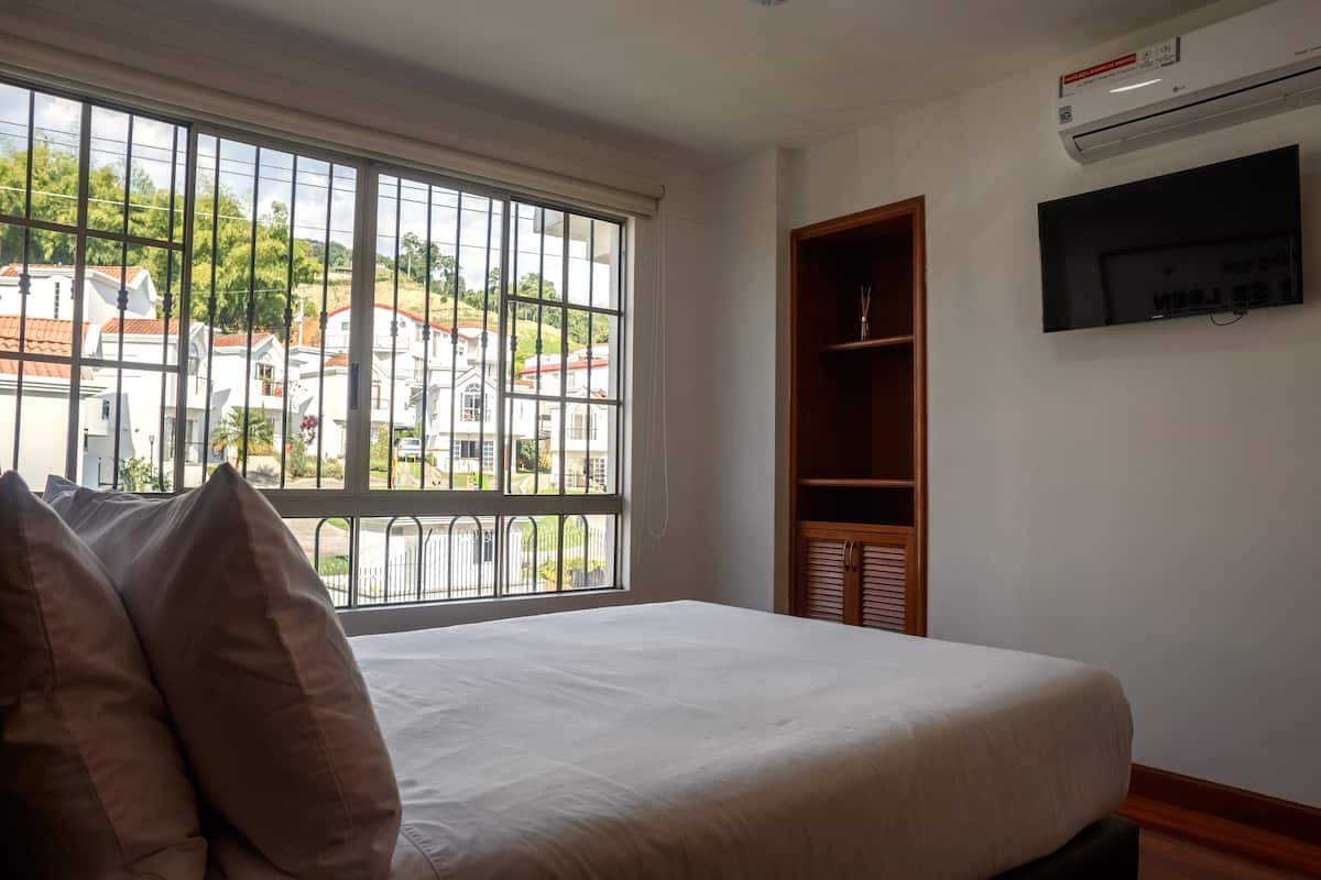 A bedroom with a large window, a bed, a TV, and a built-in wardrobe.