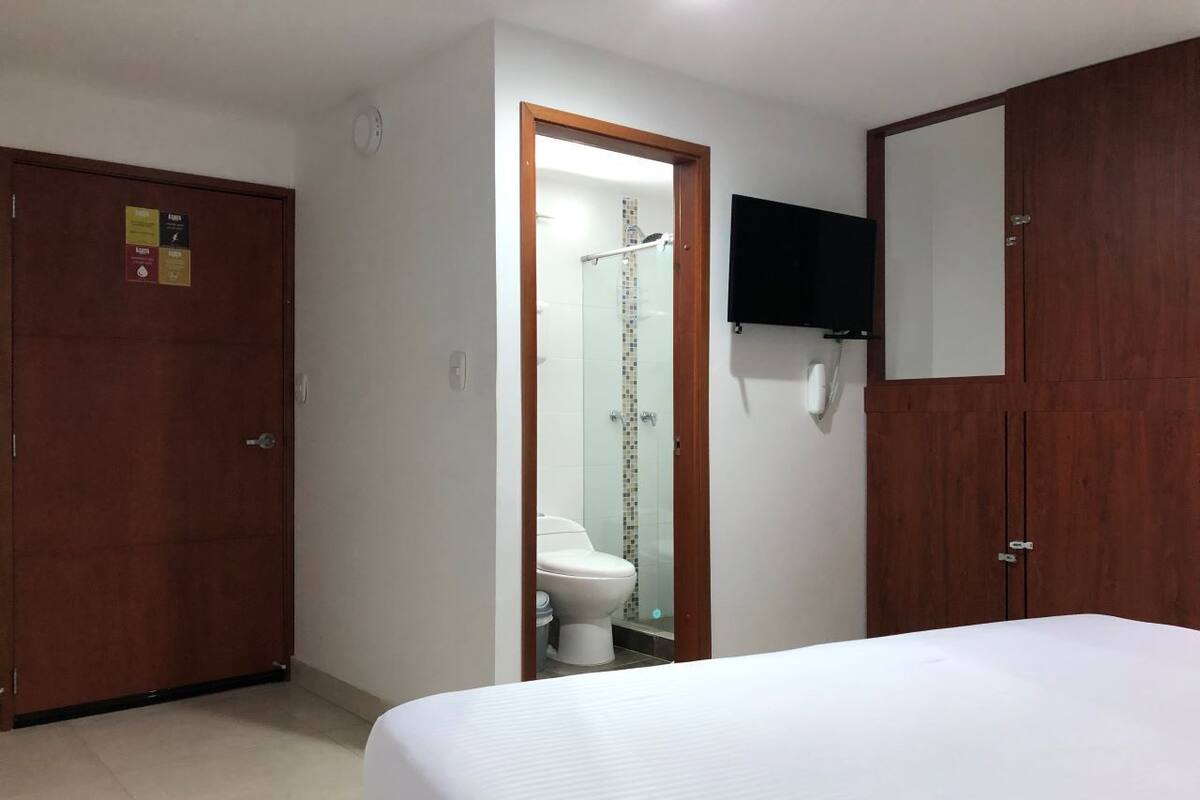 A hotel room with a bed, a wooden wardrobe, a toilet, and a shower.