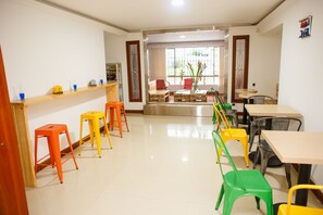 Una habitación amplia con una mesa larga y sillas, una barra de madera con taburetes, y vista a través de un ventanal.