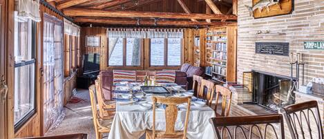 Un interior de cabaña acogedor con comedor, chimenea y estanterías.