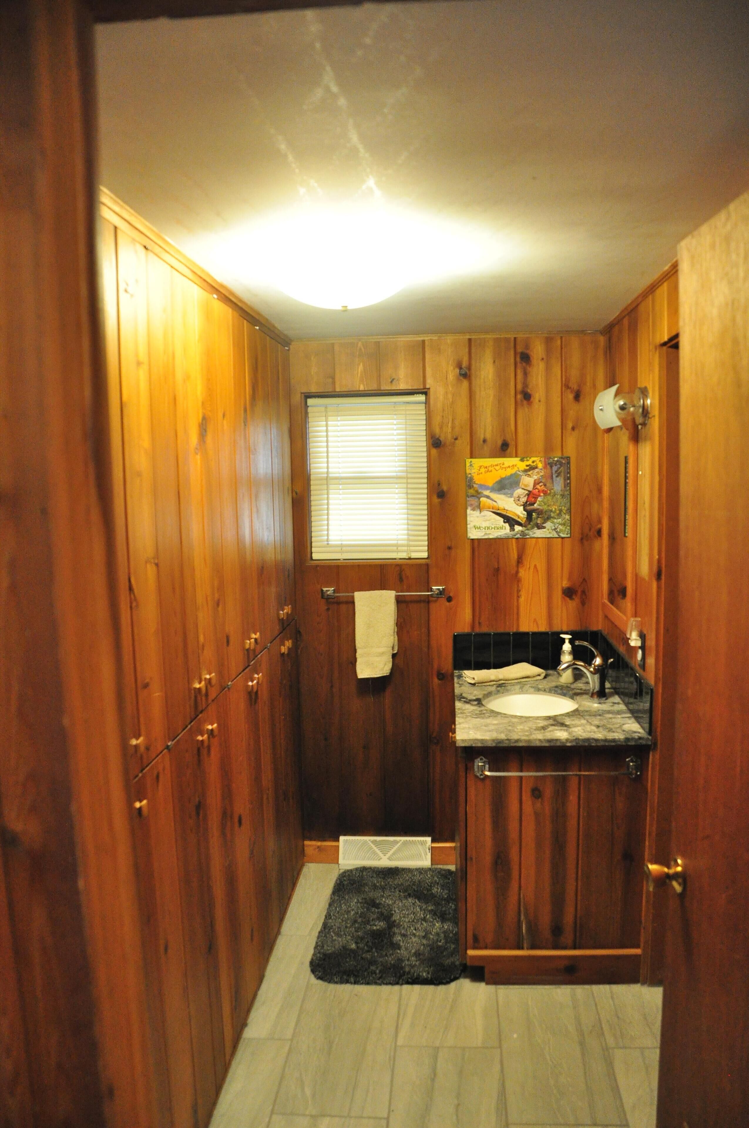 A wooden-paneled bathroom with a sink, towel rack, and a small window.