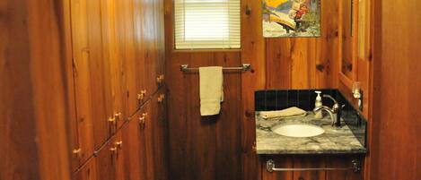 A wooden-paneled bathroom with a sink, towel rack, and a small window.