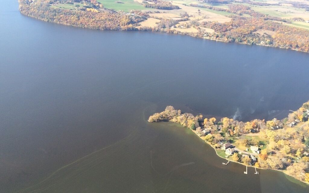 An aerial view of a lake with a small island featuring houses and trees.