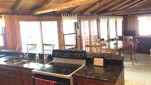 Una cocina con armarios de madera, una estufa y un lavamanos. Hay sillas y una mesa en el comedor.