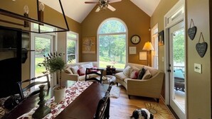 A spacious living room with a high ceiling, a dining area, and a large window providing a view of the outdoors.