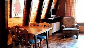 A dining area with a wooden table and chairs, a television, and a patterned armchair.