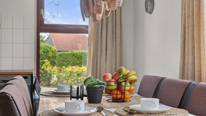 Mesa para comer dispuesta con individuales, cesta de frutas, planta en maceta y una cafetera.