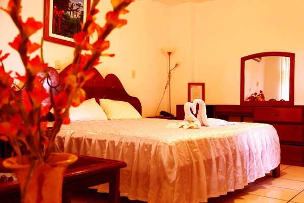 A neatly made bed with a white bedspread, a bedside table with a lamp, and a mirror on the wall.