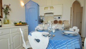 Un'area pranzo con una tovaglia a quadretti blu, sedie bianche e un armadietto blu.
