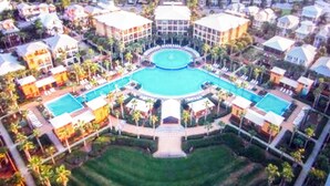 Vista aérea de un resort con una piscina central, varias edificaciones para huéspedes y jardines bien cuidados.