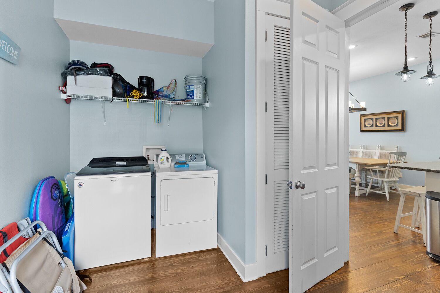 A laundry room with a washing machine, dryer, and shelves above containing various items.