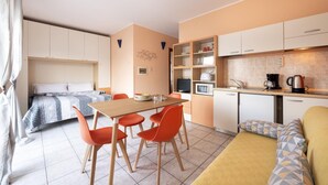 Ein kleines Hotelzimmer mit Bett, Esstisch und Stühlen, einer Küchenzeile und einem Sofa.