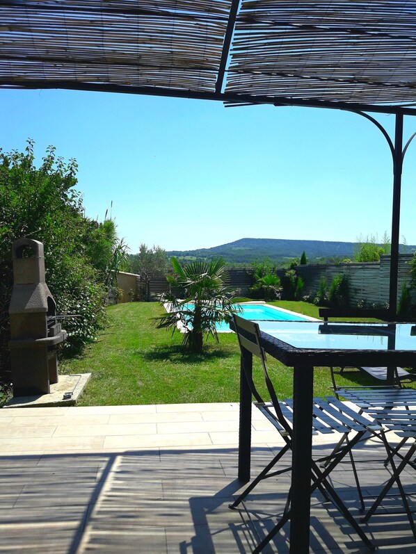 A patio area with a pool, a grill, and a view of the countryside.