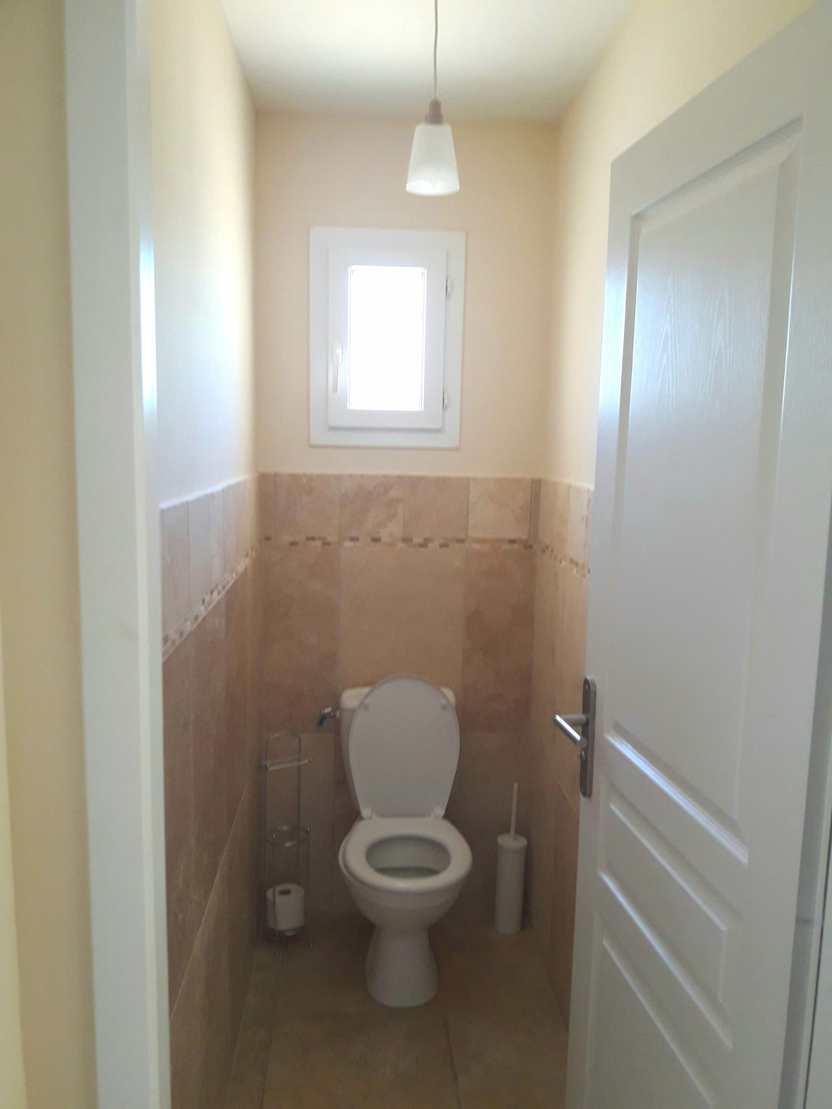 A small bathroom with a toilet, a window, and a door.