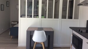 A modern kitchen with a built-in oven, a dining area with a table and chairs, and a large window with blinds. - Air-conditioned studio with charming little garden in Villeneuve les Avignon (Villeneuve-Lès-Avignon)