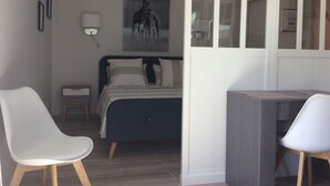A bedroom with a bed, two chairs, a desk, a nightstand, a wall-mounted lamp, and a framed picture. - Air-conditioned studio with charming little garden in Villeneuve les Avignon (Villeneuve-Lès-Avignon)