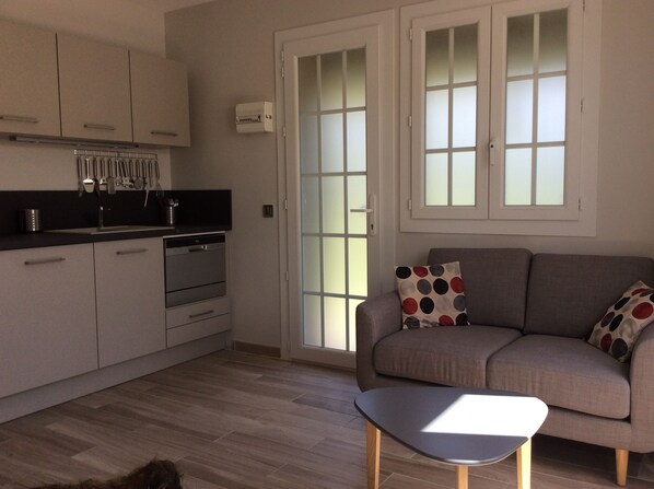 A modern kitchen with white cabinets, a built-in oven, and a black countertop. There is a grey sofa with a polka dot cushion and a small table in front.