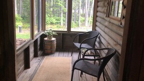 A log cabin with a porch, two wicker chairs, a small table, and a potted plant. - A Historic Storybook Maine Cottage (New Harbor)