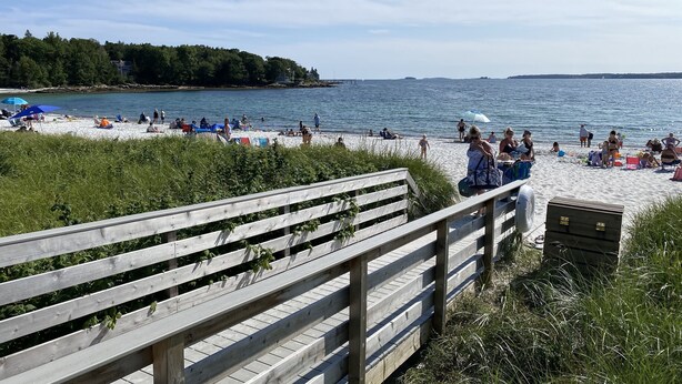 A wooden boardwalk leading to a beach with people sunbathing and swimming. - A Historic Storybook Maine Cottage (New Harbor)